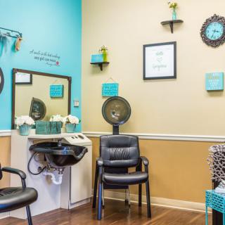 A cozy salon interior featuring a hair washing station, chairs, and decorative wall art in teal and beige tones.