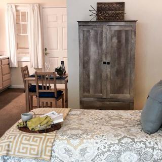 A cozy bedroom setup with a bed, wooden wardrobe, and dining area.