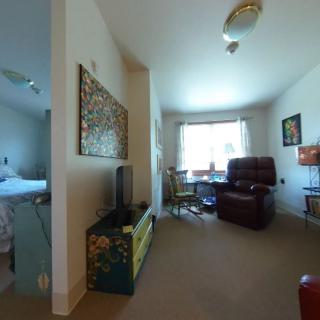 A cozy living space with an armchair, television, and a window allowing natural light in, adjacent to a bedroom.