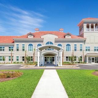 A beautifully designed building with a red-tiled roof and an inviting entrance, surrounded by a well-maintained lawn under a clear blue sky.