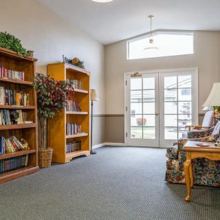 A cozy library corner with bookshelves and a comfortable seating area, illuminated by natural light from large windows.