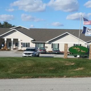 A single-story building with flags in front, surrounded by a lawn and parked cars under a partly cloudy sky.
