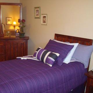 A cozy bedroom with purple bedding and a wooden dresser.