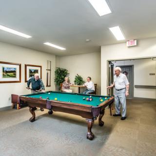 A group of seniors enjoying a game of billiards in a recreation room.