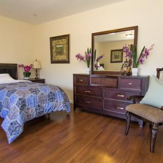A cozy bedroom with a single bed, wooden dresser and mirror, decorated with flowers and wall art.