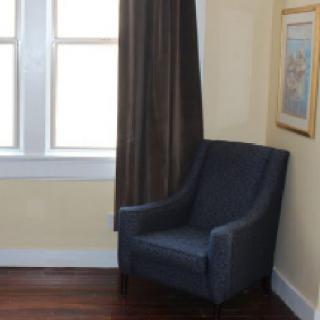 A cozy corner with a blue armchair next to a window and dark curtains, adorned with wall art.