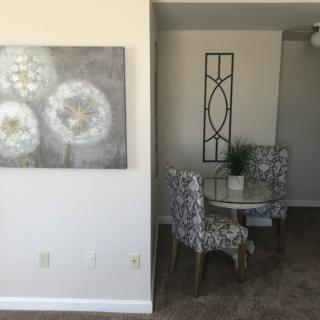 A cozy dining area featuring a round table with patterned chairs, complemented by a decorative plant and wall art.