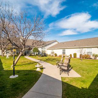 A serene courtyard with a walkway, seating area, and trees under a clear blue sky.