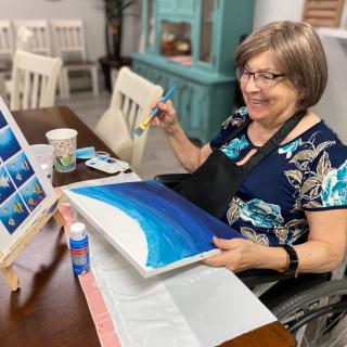 A woman smiling while painting a canvas indoors.