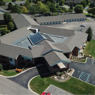 Aerial view of a building with solar panels on the roof surrounded by a parking lot and green landscape.