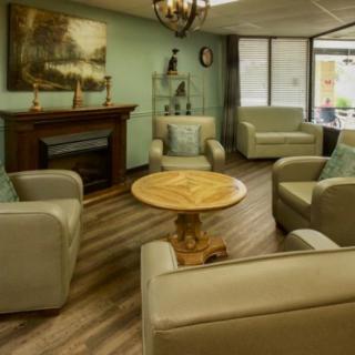 A cozy living room with comfortable armchairs arranged around a round wooden coffee table, featuring a decorative fireplace and modern decor.