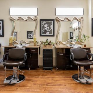 A stylish hair salon interior featuring two barber chairs and ornate mirrors on a wooden floor.