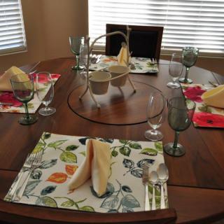 A neatly set dining table with floral placemats, folded napkins, and glasses.