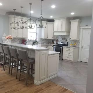 A modern kitchen with white cabinets and a central island featuring bar stools and chandeliers.