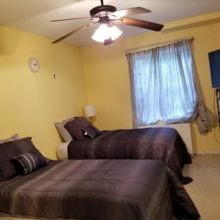 A cozy bedroom with two beds, featuring a ceiling fan and yellow walls.