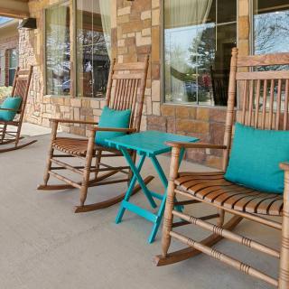 A cozy porch featuring wooden rocking chairs with turquoise pillows and a small table against a stone wall backdrop.