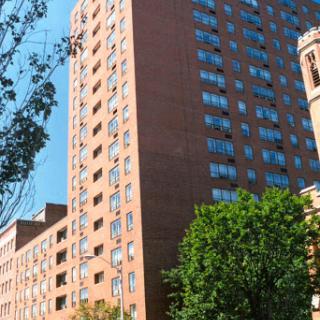 A tall brick apartment building surrounded by trees under a clear blue sky.