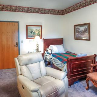 A cozy bedroom featuring a hospital bed, comfortable armchair, and decorative artwork on the walls.