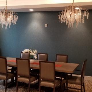A modern dining room with elegant chandeliers and a long table surrounded by chairs.