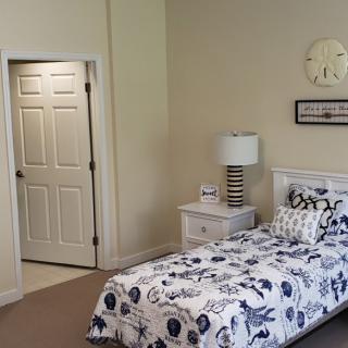 A cozy bedroom with a single bed, nightstand, and decorative lamp beside it. A door is visible to the side.