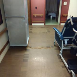 A view of a hospital corridor with a wheelchair and refrigerator.