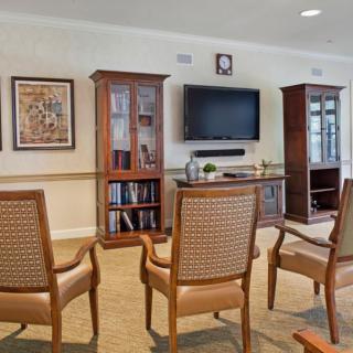 A cozy living room with a seating area, featuring four chairs facing a television mounted on the wall and flanked by cabinets and bookshelves.