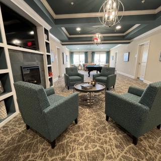A cozy lounge area with four armchairs arranged around a circular table and a grand piano in the background.