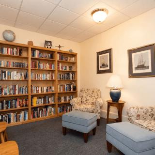 A cozy reading room with a bookshelf filled with books, comfortable chairs, and a lamp.