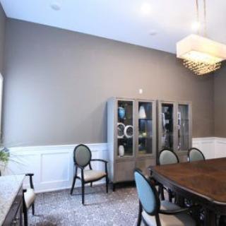 A modern dining room featuring a large wooden table, upholstered chairs, a decorative cabinet, and a stylish chandelier.