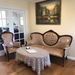 A cozy living room featuring vintage furniture including an antique sofa and armchair, complemented by a lace-covered coffee table and elegant wall art.