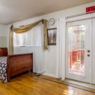 A cozy bedroom with a wooden bed, decorated curtains, a white framed door, and a clock on the wall.