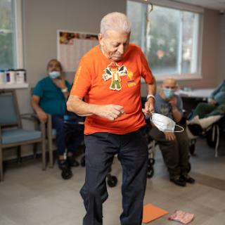 An elderly man participates in a fun activity at a community center, promoting physical movement and social interaction.