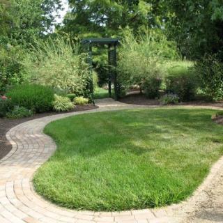 A beautifully landscaped garden with a curved pathway, lush green lawn, and an archway leading to a secluded area.