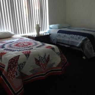 A cozy bedroom with two beds featuring colorful quilts and window blinds.