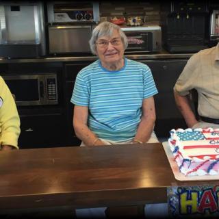 A group of people sitting at a table with a patriotic-themed cake, celebrating an occasion.