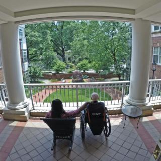 Two people enjoying a peaceful view from a balcony overlooking a garden.