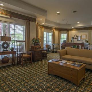 A cozy and elegantly furnished living room with a large couch, wooden tables, and ample natural lighting.