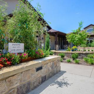 A beautifully landscaped garden with a stone wall and vibrant flowers, leading up to a house on a sunny day.