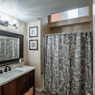 A well-decorated bathroom with a large mirror, elegant lighting, and patterned shower curtain.