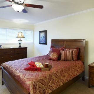 A cozy bedroom with a wooden bed and matching furniture, featuring warm bedding and a decorative lamp.