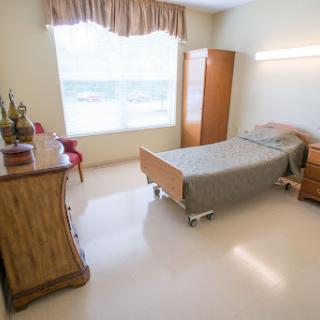 A well-lit hospital room featuring a single bed, a dresser, and a chair near the window.