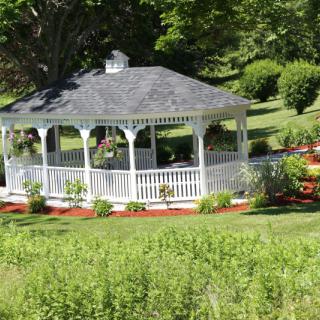 A charming white gazebo surrounded by lush greenery in a picturesque garden setting.