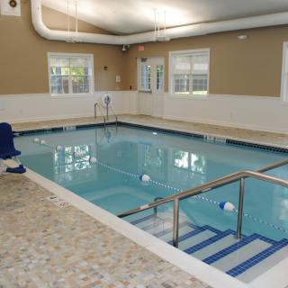 An indoor swimming pool with steps and a handrail, surrounded by windows.