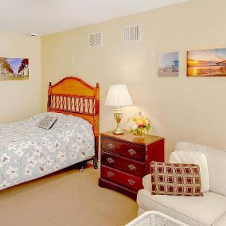 A cozy bedroom with a wooden bed, patterned bedding, a lamp on a dresser, and artwork on the walls.