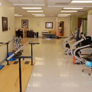 A spacious rehabilitation room equipped with various exercise machines and parallel bars.