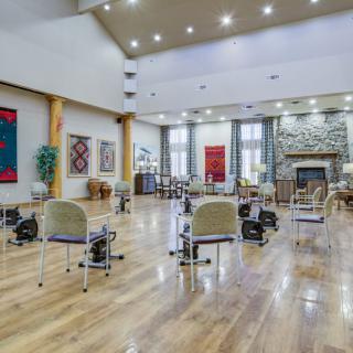 A spacious room with hardwood flooring, arranged chairs, large windows, and decorative artwork on the walls.