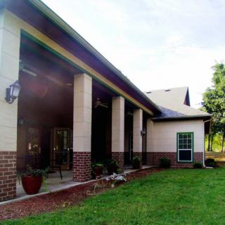A view of a house exterior with brick and siding, featuring a spacious porch and lawn.