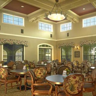 A spacious and elegantly decorated dining area with multiple tables and chairs, featuring large windows and a central chandelier.