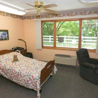 A cozy bedroom with a single bed, a recliner, and large windows overlooking greenery.