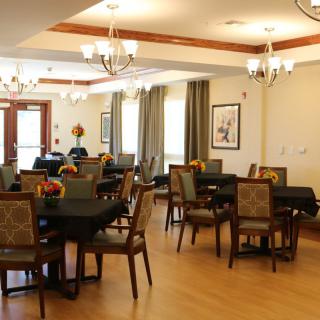 An elegant dining area with multiple tables and chairs, adorned with chandeliers and warm lighting.